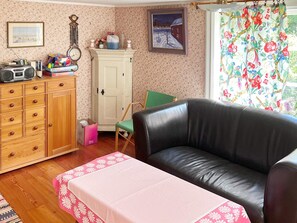 A living room with a black leather sofa, a wooden cabinet with drawers, a green chair, and a table with a pink floral tablecloth. - 7 Person Holiday Home in Algaras (Älgarås)