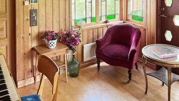 A wooden room with a piano, a chair, a table with a book, and a vase with flowers.