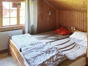 Een kamer met houten lambrisering, een bed, een raam met gordijnen en een wandlamp.