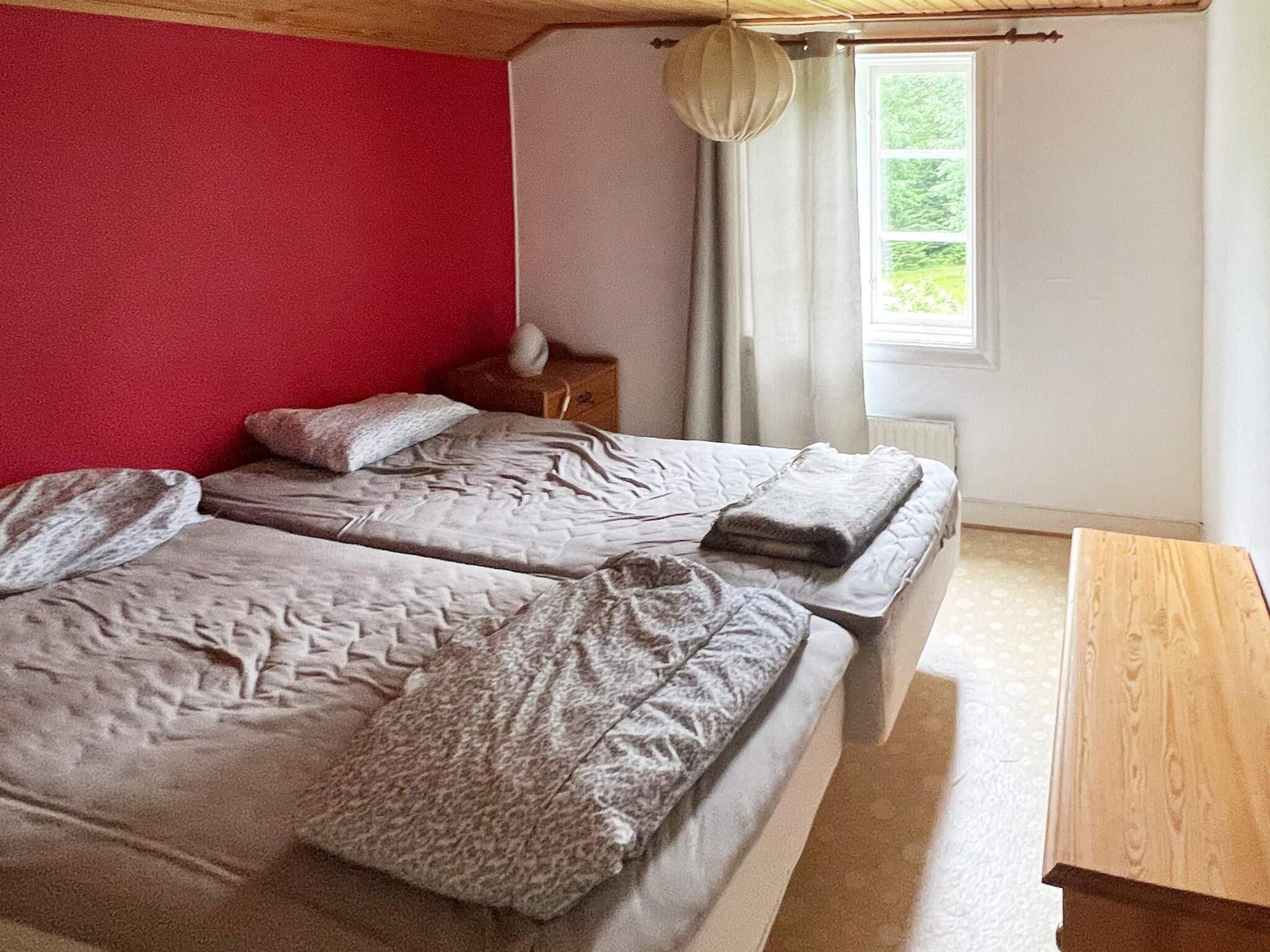 Een slaapkamer met twee bedden, een houten nachtkastje, een raam met gordijnen en uitzicht op groen buiten.
