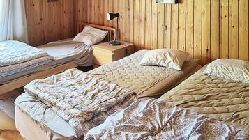 A room with three beds, wooden walls, and a nightstand with a lamp.