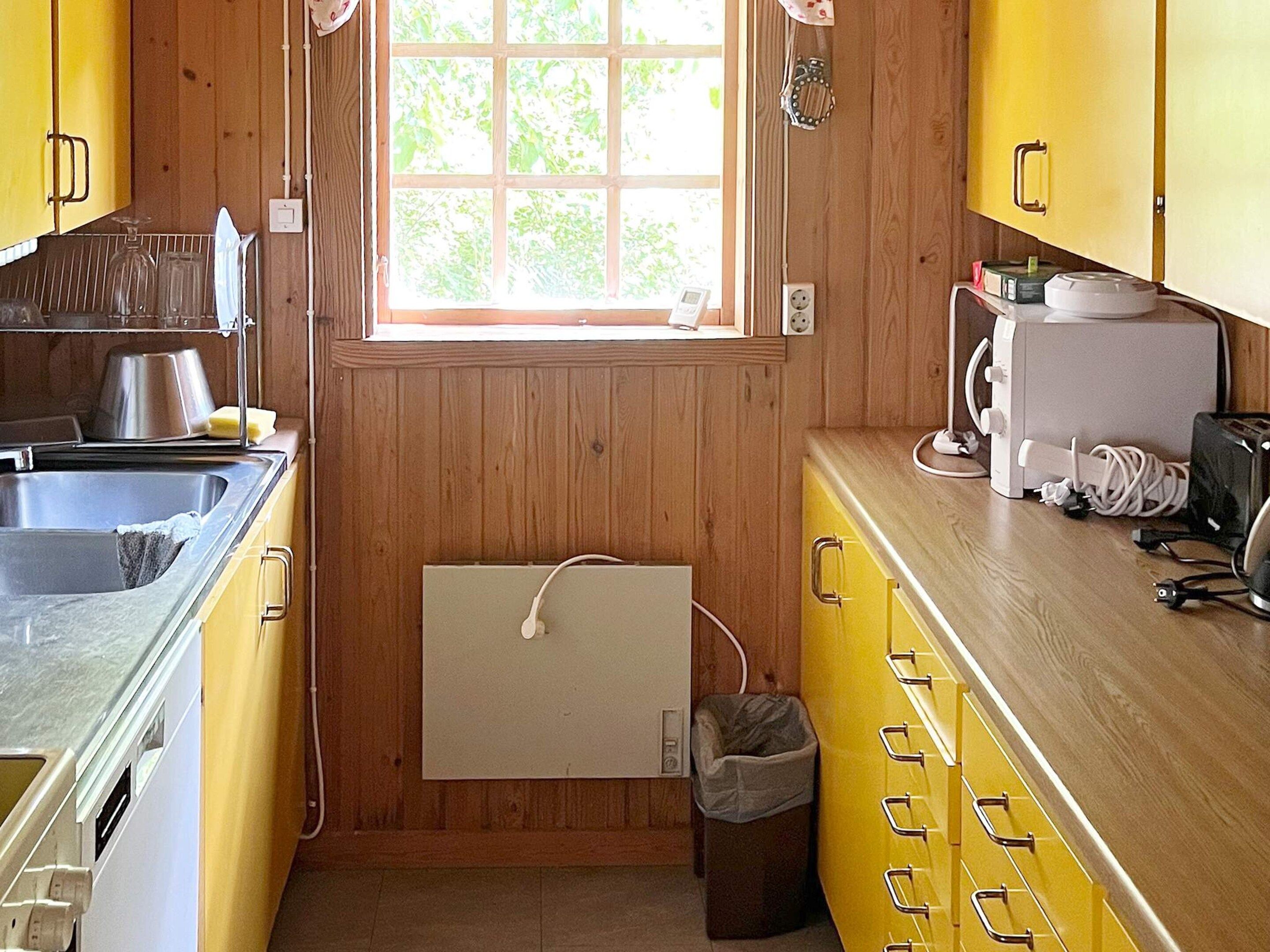 Cocina compacta con paredes de madera, una ventana, un lavabo, una estufa y un cubo de basura.