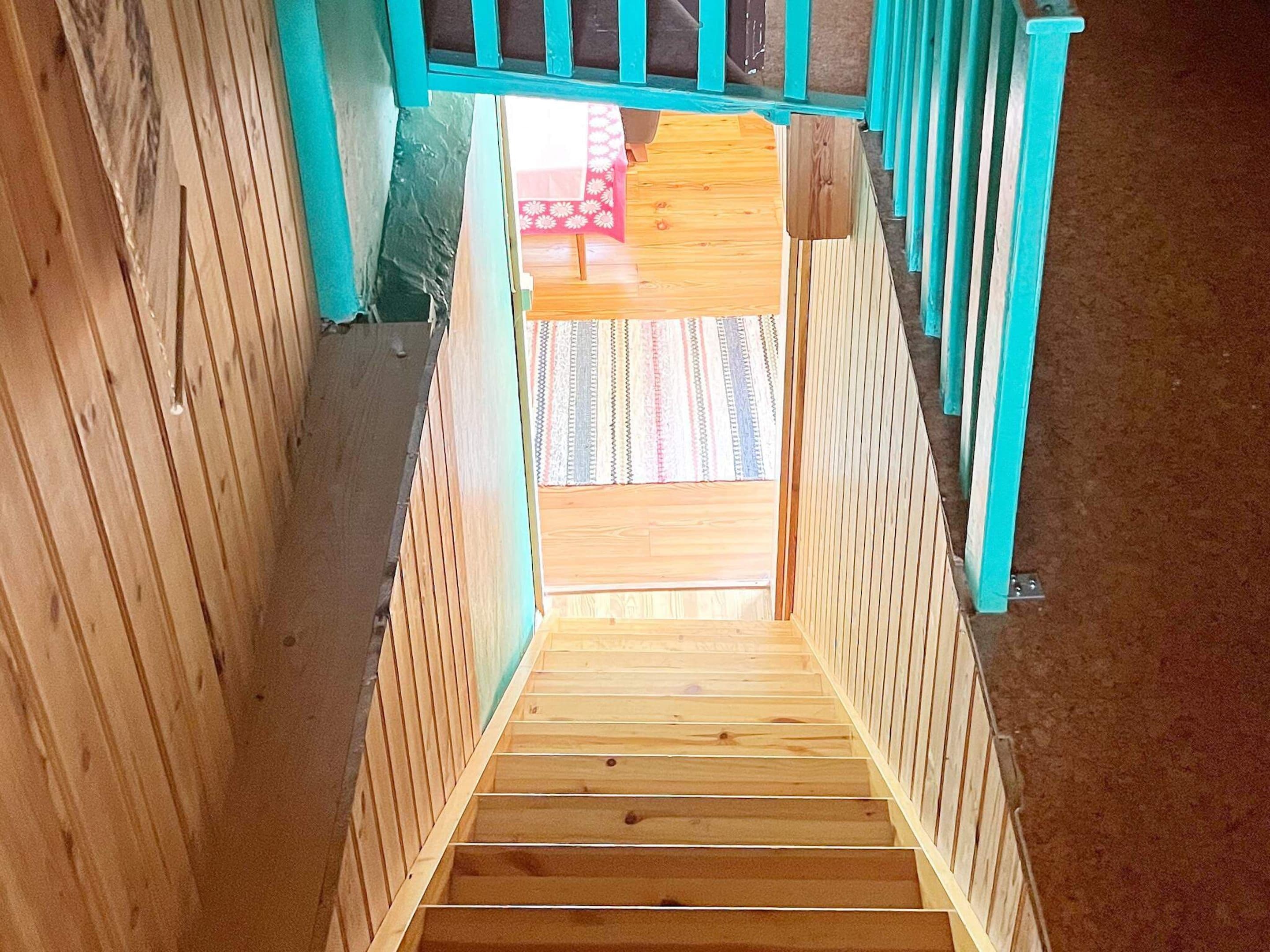 A wooden staircase with a view of a patterned rug and a red object in the background.