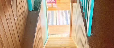 A wooden staircase with a view of a patterned rug and a red object in the background.