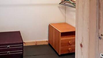A small room with a wooden nightstand, a dark-colored dresser, and a wall-mounted shelf with hangers.