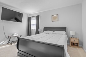 Una camera da letto moderna con un letto, comodini, una TV a parete e una finestra con tende.