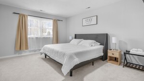 Een slaapkamer met een bed, nachtkastjes, een raam met gordijnen en een bord aan de muur.