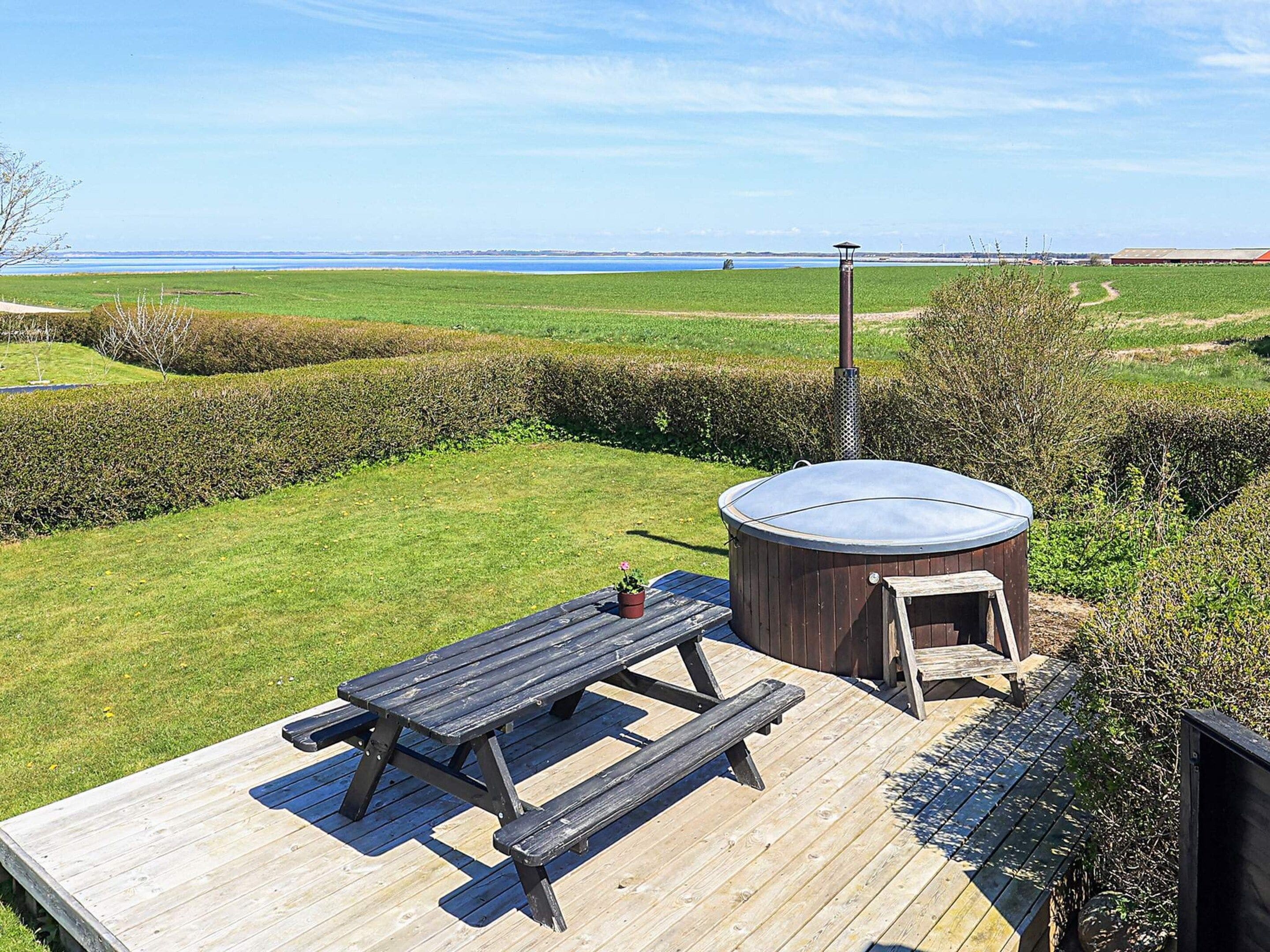 A wooden deck with a hot tub, picnic table, and a view of the sea.