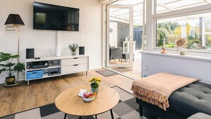 A modern living room with a flat-screen TV, a sofa, a round coffee table, and a window with a view of greenery. - 6 Person Holiday Home in Vinderup (Vinderup)