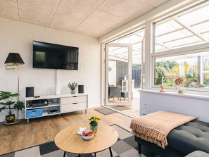 A modern living room with a flat-screen TV, a sofa, a round coffee table, and a window with a view of greenery. - 6 Person Holiday Home in Vinderup (Vinderup)