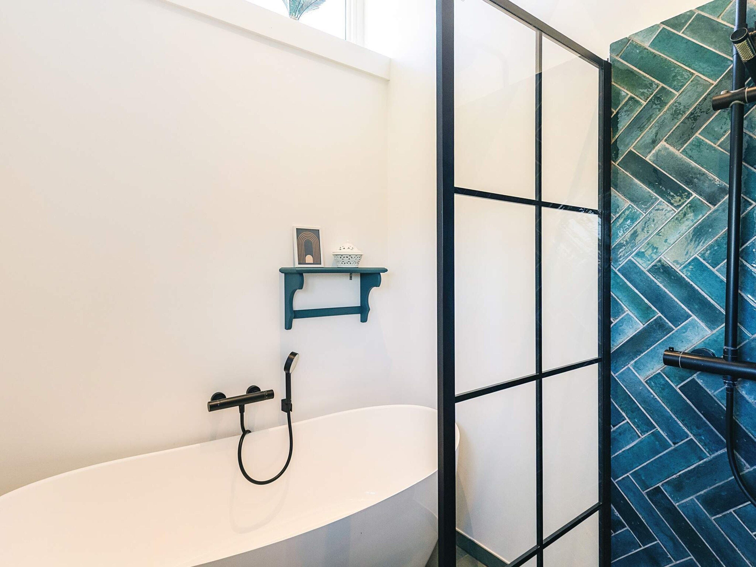 A modern bathroom with a white bathtub, a shower enclosure, and a blue shelf with a framed picture.