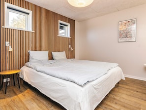A bedroom with a bed, two windows, a wall-mounted light, a small table, and a framed picture. - 6 Person Holiday Home in Vinderup (Vinderup)