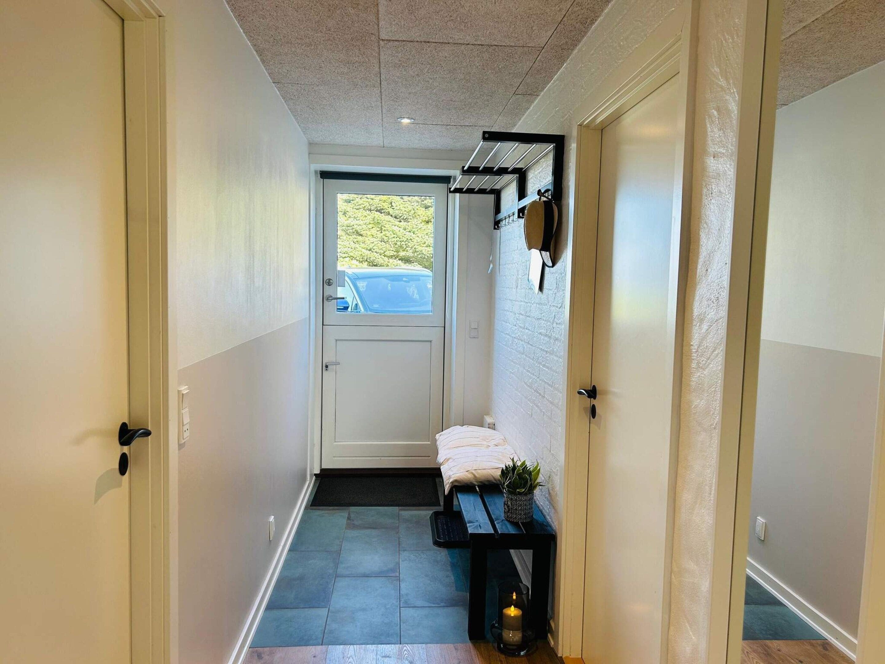 A narrow hallway with a bench, a small table with a candle, and a door leading to a room.