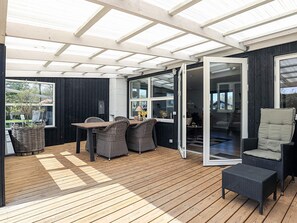 A covered patio with a wooden table and wicker chairs, a glass door leading to an interior space, and a view of the outdoors. - 6 Person Holiday Home in Vinderup (Vinderup)