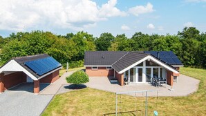 Um edifício com painéis solares no telhado, um alpendre com área de estar ao ar livre e um pequeno jardim.