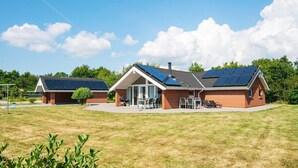 Uma casa com fachada de tijolo, um alpendre com mobiliário de exterior e painéis solares no telhado.