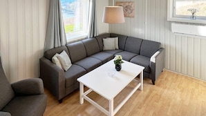 A living room with a grey sectional sofa, a white coffee table, and a window with curtains. - 4 Person Holiday Home in Sundlandet-by Traum (Hitra)