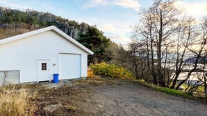 A white building with a garage door, surrounded by a gravel driveway and a forested area with a mountain in the background. - 4 Person Holiday Home in Sundlandet-by Traum (Hitra)