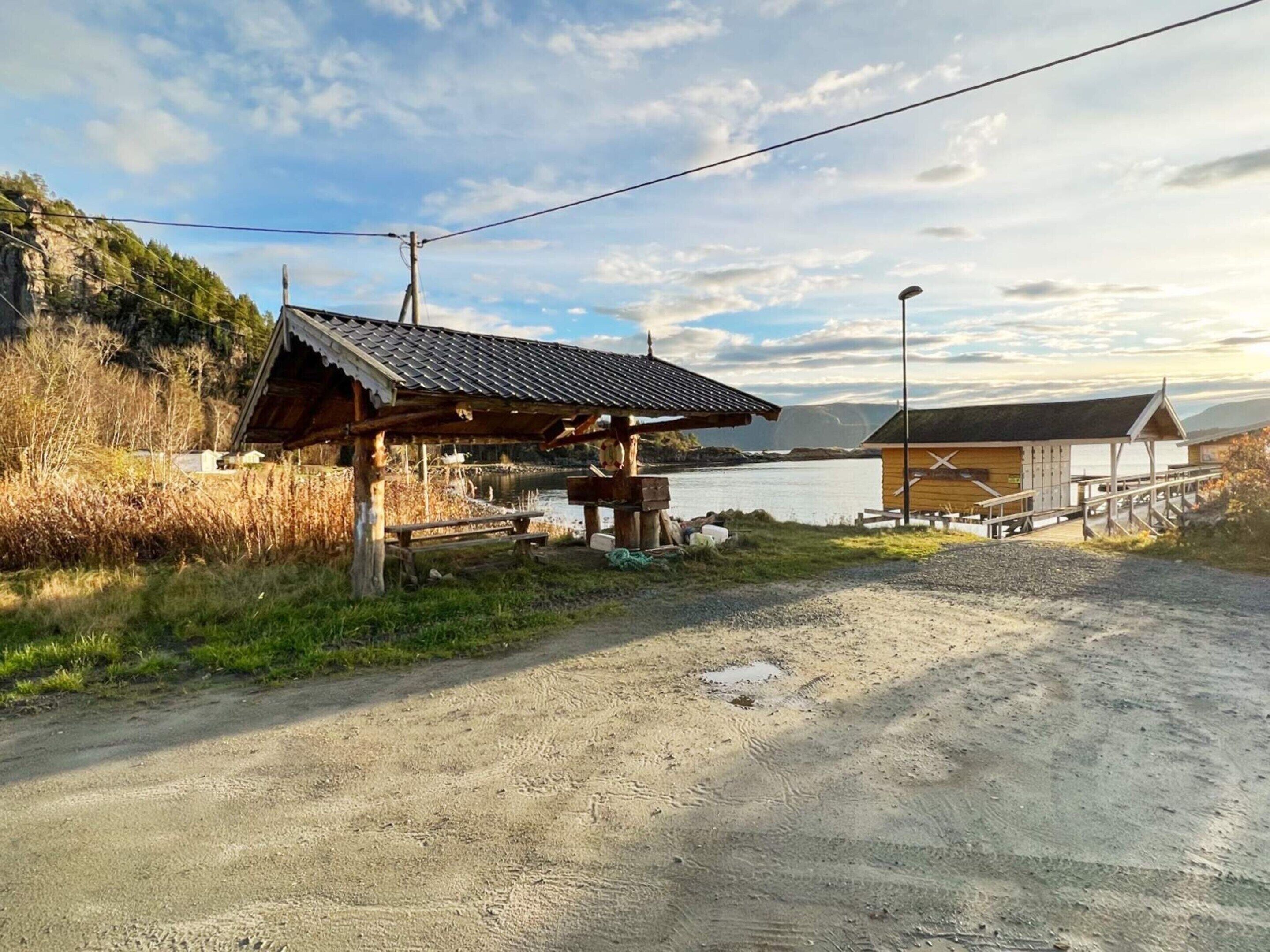 A rustic wooden cabin with a metal roof, a wooden pier extending into a lake, and a clear sky.