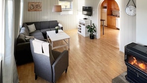 A cozy living room with a sofa, a small table, a fireplace, and a kitchen visible through an archway. - 4 Person Holiday Home in Sundlandet-by Traum (Hitra)