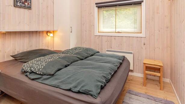 A bedroom with a bed, a bedside table, a window, and a wall-mounted picture. - 6 Person Holiday Home in Farso (Farso)