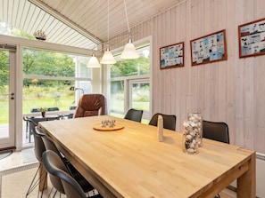 A dining area with a wooden table, chairs, pendant lights, and a view of the outdoors.