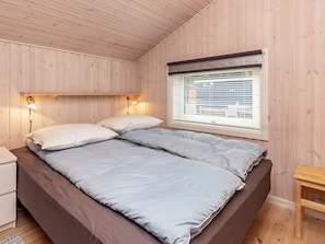 En seng med sengegavl, to sengeborde med lamper, et vindue med skodder og et trænatbord.