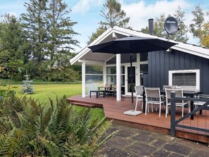 A modern outdoor deck with a table and chairs, surrounded by a garden and trees. - 6 Person Holiday Home in Farso (Farso)