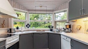 A modern kitchen with a built-in oven, a coffee machine, and a view of greenery through large windows. - 6 Person Holiday Home in Farso (Farso)