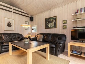 A modern living room with two leather sofas, a wooden coffee table, a television, and a bookshelf.