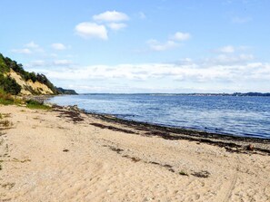 En sandstrand med et roligt hav, en klar himmel og land i det fjerne.