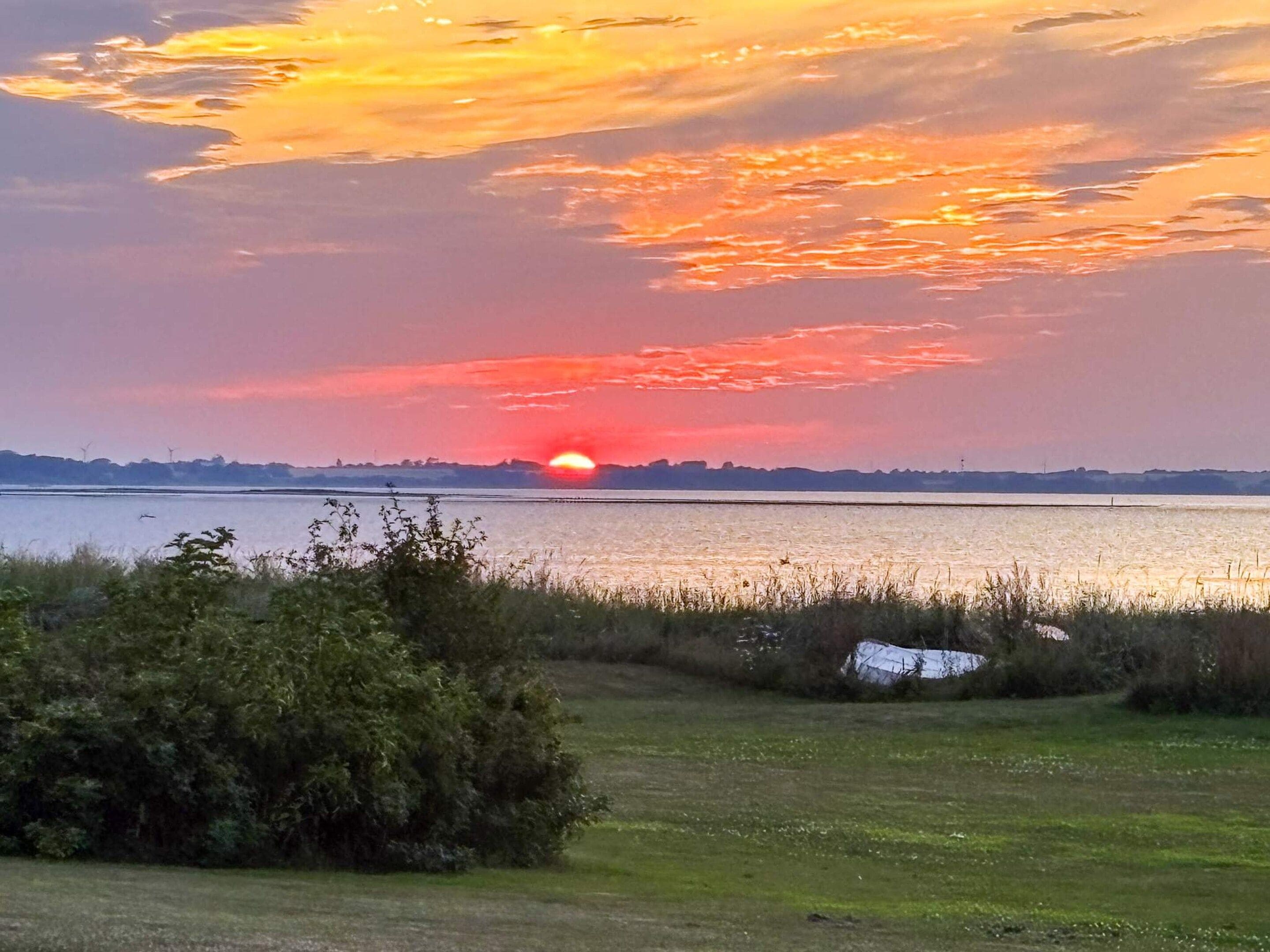Un coucher de soleil sur une étendue d’eau, avec une côte lointaine et des éoliennes.