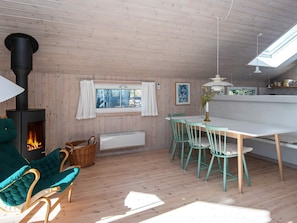 L’intérieur d’un chalet accueillant, avec un poêle à bois, un coin repas comprenant des chaises et une table, et une vue par la fenêtre.