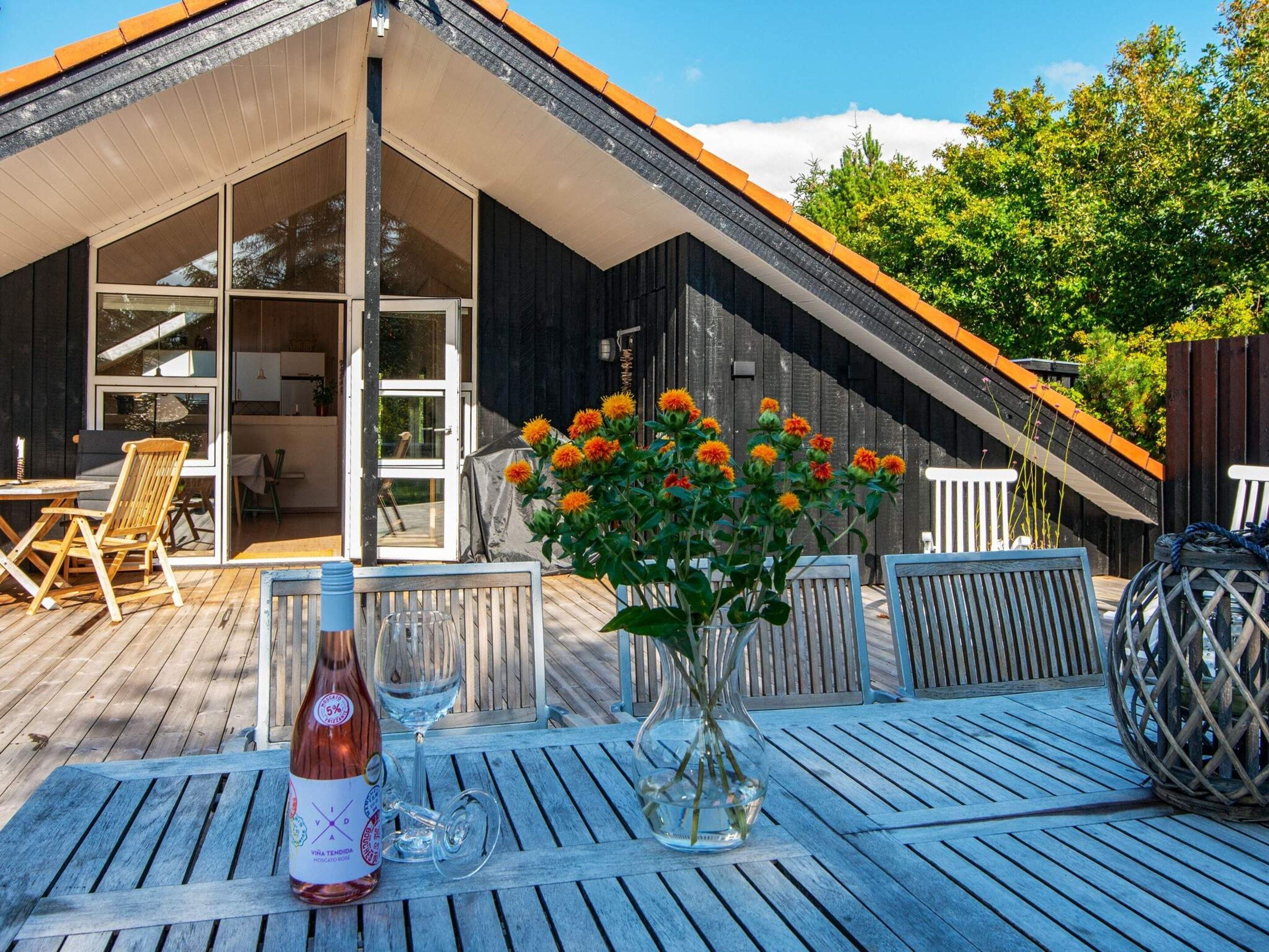 A wooden deck with outdoor furniture, a bottle of wine, and a vase with flowers.