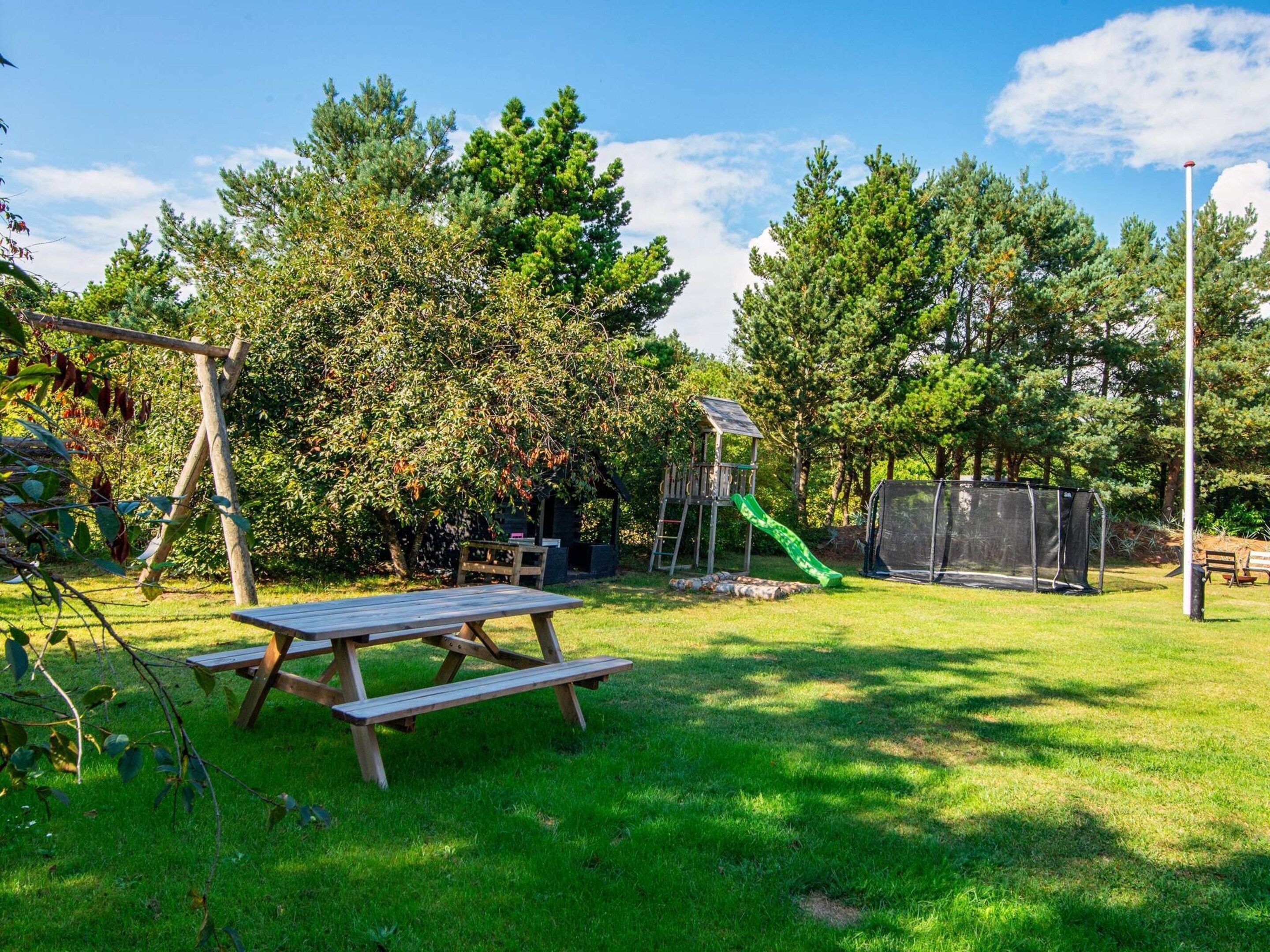 A picnic table in a grassy backyard with a play structure and a slide.