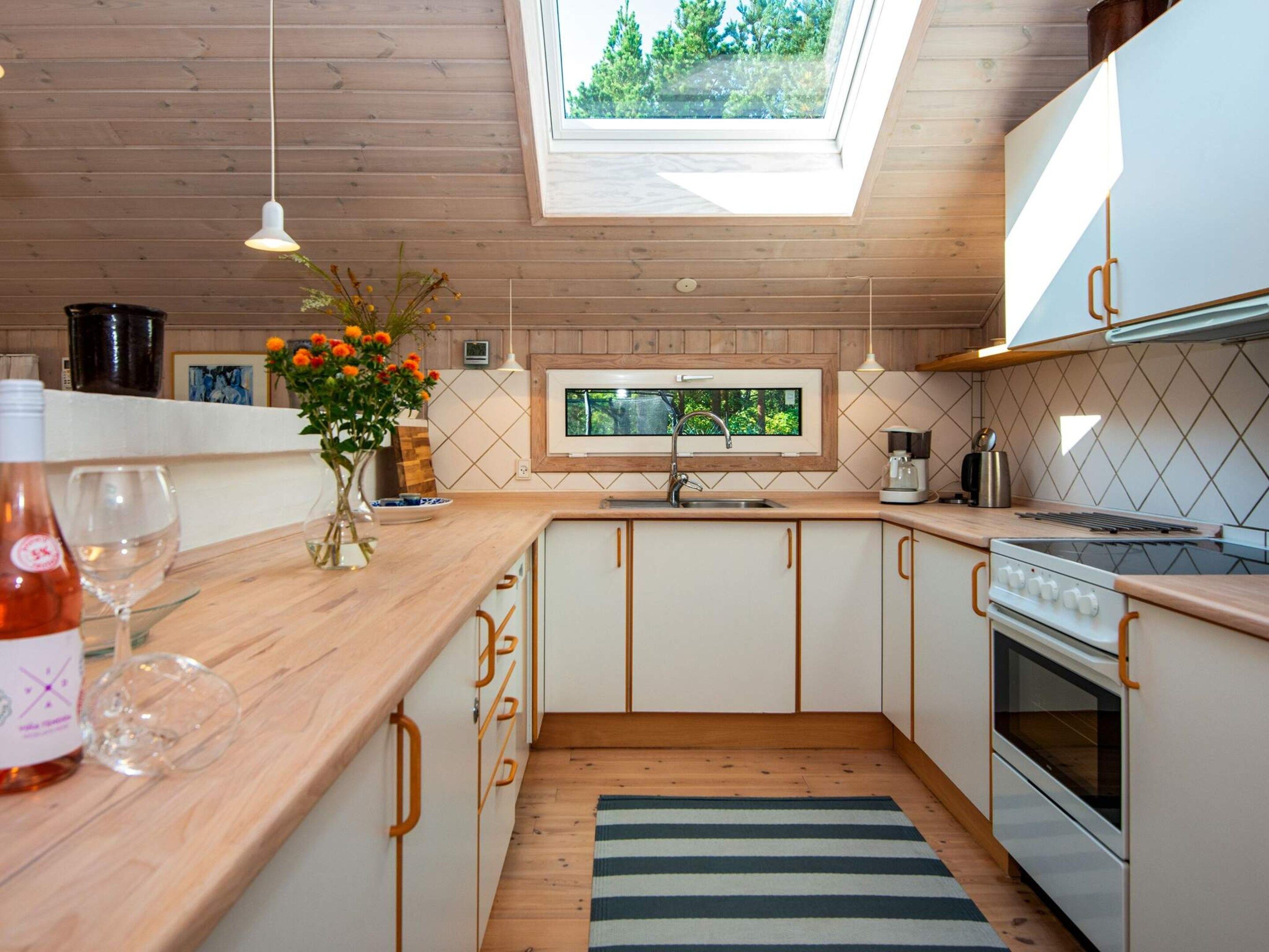 A modern kitchen with wooden cabinets, a skylight, and a view of greenery outside.