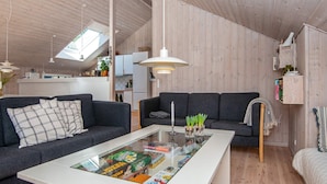 Uma sala de estar moderna com dois sofás escuros, uma mesa de centro de vidro e piso de madeira.