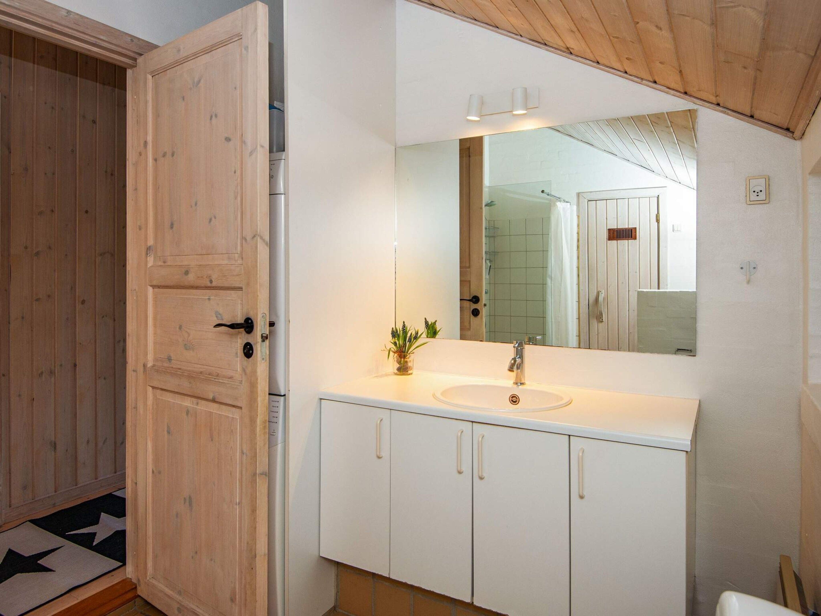 A bathroom with a wooden door, white cabinets, a sink, and a mirror.