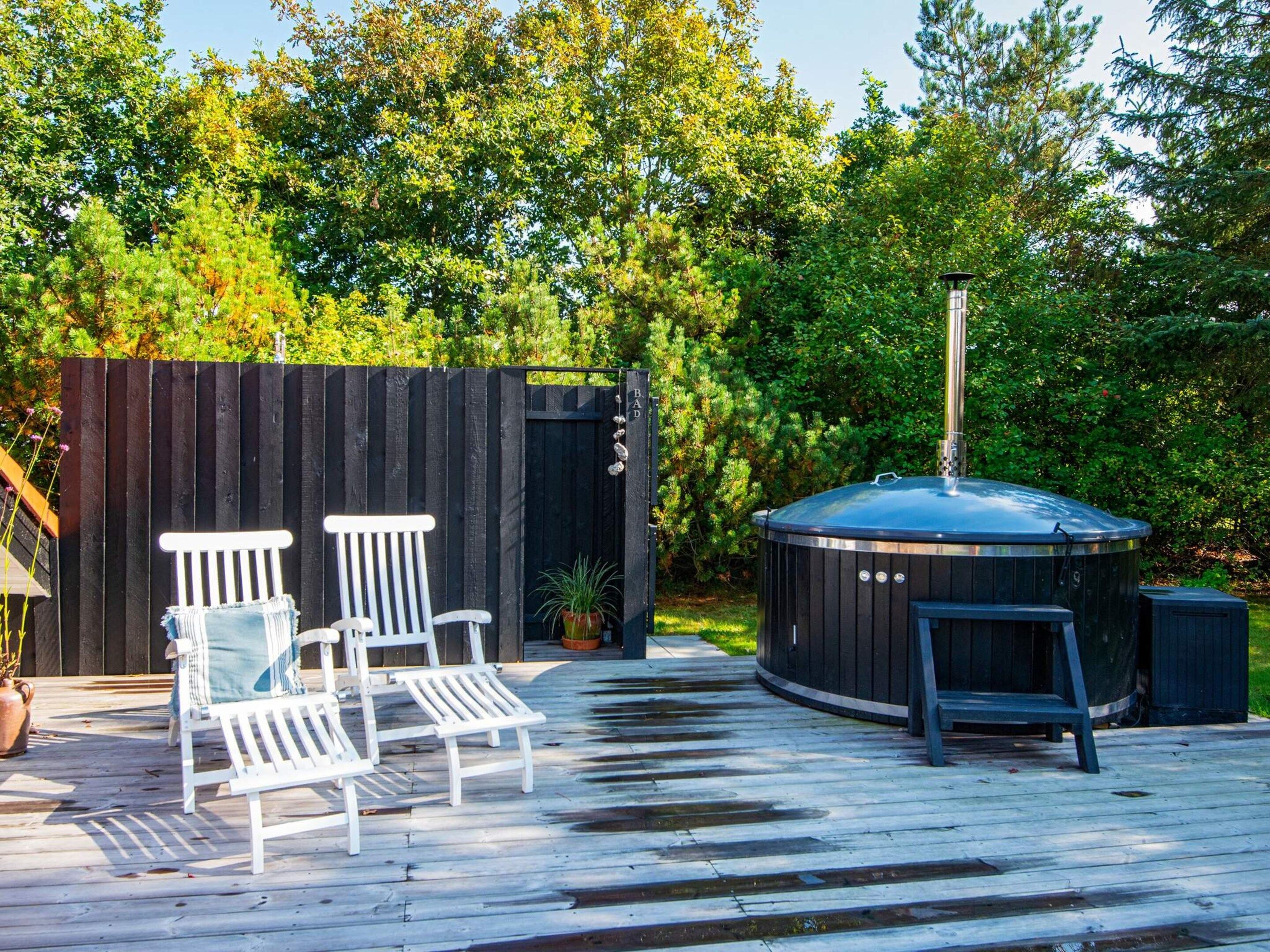 A wooden deck with two white chairs and a hot tub.