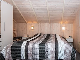 Un dormitorio con cama, mesitas de noche, una silla y paredes de madera.