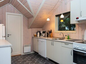 Uma cozinha compacta com paredes de madeira, bancada branca, forno embutido e janela com vista para árvores.