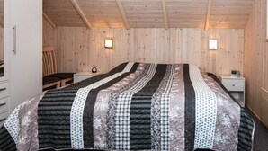 A bedroom with a large bed, wooden walls, two bedside tables, and a chair.