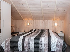 Un dormitorio con una cama grande, paredes de madera, dos mesitas de noche y una silla.