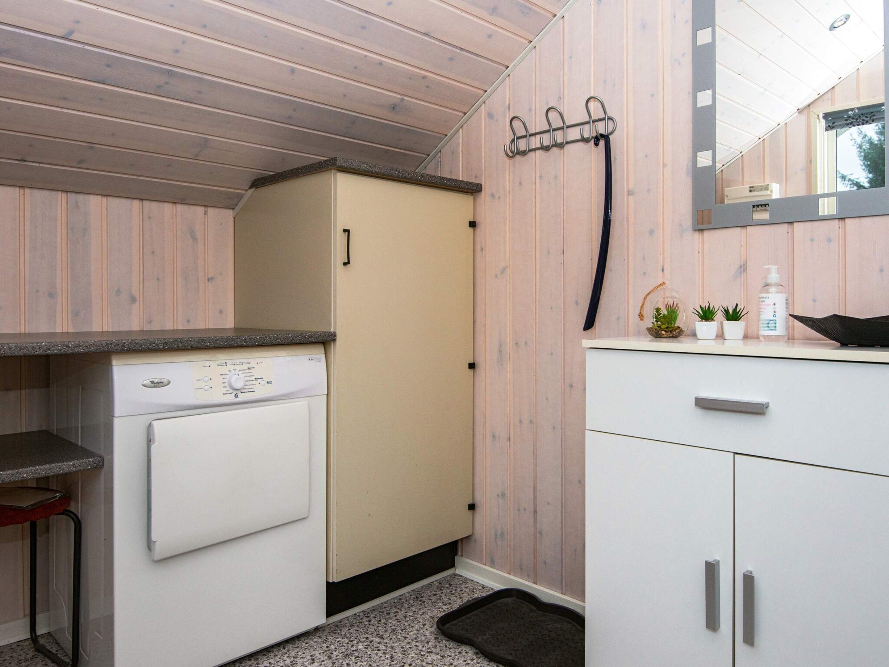 A compact kitchen with a washing machine, a sink, and a small countertop with plants and toiletries.