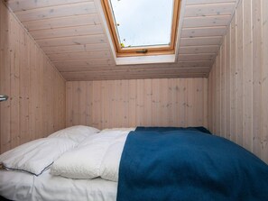 Quarto com teto inclinado, paredes de madeira, claraboia e cama com roupa de cama branca e azul.