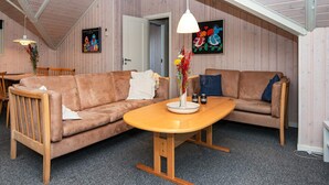 A cozy room with a wooden ceiling, a brown sofa, a wooden table, and a hanging light fixture.