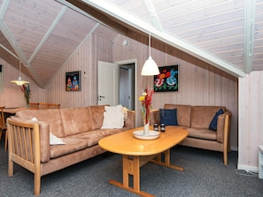 Una habitación acogedora con techo de madera, un sofá marrón, una mesa de madera y una lámpara colgante.