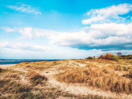 Un paisaje costero con dunas, cielo despejado y una vista distante del mar.
