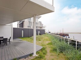 Una terraza moderna al aire libre con vista a un cuerpo de agua y un edificio al fondo.