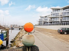 Un puerto deportivo con barcos, un edificio moderno con balcones y un coche aparcado al lado.